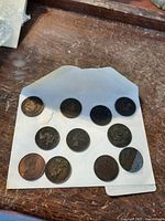 Photo of all 11 collectible coins arranged on a white paper on a wooden surface, showing various sizes and designs including a half broken coin.