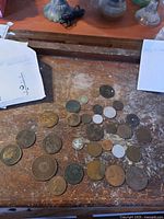 View of 30 assorted collectible coins on a wooden surface showing range of sizes and colors.