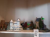 Six Thomas Kinkade Hawthorne Village houses displayed together on a marble shelf showing variety in styles and decorations.