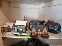 Overview of five of the seven lighted village buildings on shelf, winter scene.