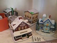 Front view of three snow-covered Christmas village buildings, including General Store, theater, and one other building