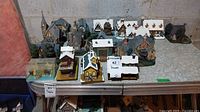 Overview of all 16 buildings and 2 dog figurines on table against cinder block wall