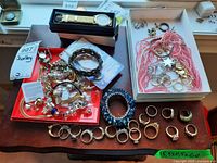 Overview of assorted jewellery including rings arranged in front, bracelets and necklaces on trays