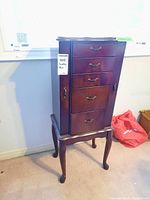 Front view of dark wood jewelry cabinet with four drawers and two doors on slender curved legs.