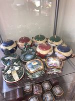 Front view of assorted Thomas Kinkade music boxes showing colorful domed lids and miniature garden scenes.