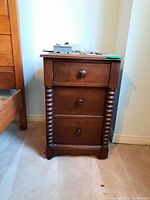 Front view of wooden nightstand showing three drawers with round knobs and turned columns on corners.