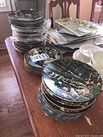 Photo showing multiple stacks of decorative plates including cat and floral designs, bowls, and small plates on a wooden table