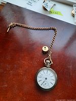 Waltham pocket watch with attached chain and bullet-shaped pendant on a wood surface