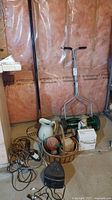 Full view of the lot items including the Scotts reel mower with metal handle, various baskets, ceramic pitcher, extension cords, power bar, composite figure, and coiled wire.
