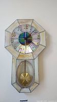 Front view of octagonal stained glass clock showing iridescent and cream glass panels, gold numerals, and black clock hands.