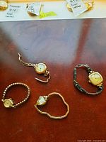 Four vintage wristwatches positioned on wooden surface, showing variety of watch face shapes and metal bands.