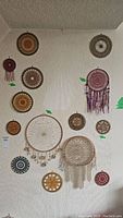 Full wall view showing a variety of circular bead art dreamcatchers and hoops including different sizes and styles hung on textured white wall.