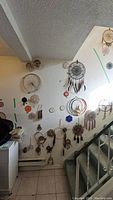 Wall display of various beaded hoops and dreamcatchers hung on wall by staircase, showing range in sizes and feather embellishments.
