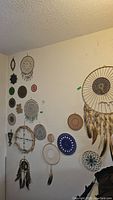 Wall display of multiple bead art hoops including dreamcatchers with feathers in varied sizes and colors.