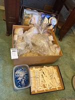 Wide view of the box containing various wrapped clear beads, spools of ribbons, a plastic container with blue and clear beads, and wooden bird craft shapes spread around.