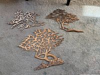 Overall view of three mid-century modern brass bonsai tree wall art pieces on carpet.