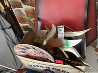 Box filled with multiple abstract brass wall art pieces with sharp curved shapes and a colorful glass plate with floral abstract design.