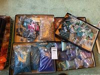 Overview of many bags of assorted small colorful craft beads in clear plastic bags spread in trays and bags.