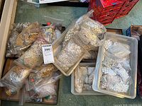 Plastic bins filled with multiple resealable bags of assorted beads, mostly white and faux pearl-like beads, with some gold tones visible in bags.
