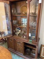 Wide shot of wooden china cabinet filled with assorted crystal and glass plates, bowls, platters, and glassware items on shelves.