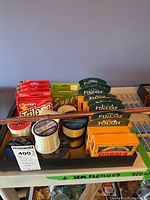 Tray with multiple fishing line spools and packages, bamboo fishing rod laid across the top, various brands visible including Maxsola and Berkley Trilene.