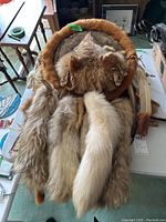 Photo showing the full wall hanging with various fur tails, fur trim, and feathers attached to a circular leather base.