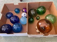 Two cardboard boxes showing multiple glass globes in blue, green, white, purple and amber tones in varying sizes.