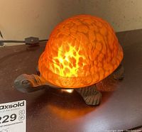 Lamp lit on a flat surface showing amber-textured glass turtle shell and dark metal turtle body base.