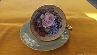 Front view of teacup seated on saucer showing full floral design and gold trim