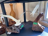 Two John Perry bird sculptures side by side on a shelf, showing white ceramic birds and resin bases