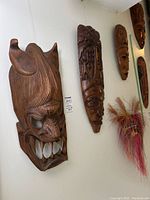 Four masks hanging on wall, three wooden and one woven grass with dyed fibers