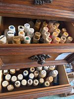 Top drawer with multiple small plastic bottles of craft acrylic paint labeled on lids with colors like sealer, yellow, green, black.