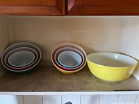 Several nested brightly coloured Pyrex bowls on a kitchen counter showing different sizes and colours.