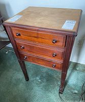 Front view of wood sewing table showing three drawers with round wooden knobs and vertical fluted leg detailing.