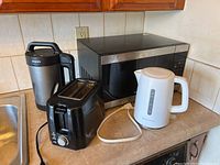 Black and stainless steel Galanz microwave, black Philips soup maker with handle, black Betty Crocker 2-slot toaster, and white Toastmaster kettle on kitchen counter.