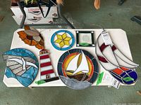 Top-down view of six stained glass wall hangings arranged on a white table, showing various nautical and geometric designs.