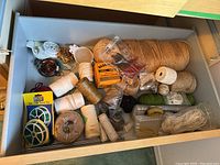 Drawer view with many spools and bundles of string and twine in natural, white, green, and brown colors including packaged twist ties.