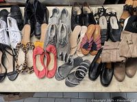 Top-down view of all 19 pairs of assorted women's shoes laid on table showing various styles including sneakers, heels, sandals, and boots in mostly neutral colors.