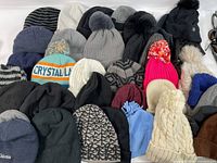 Full view of assorted beanies in different colors, some with pom-poms, various knit styles including branded items like Columbia and colorful designs.