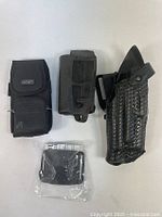 Photo showing three black assorted holsters and one sealed Gould & Goodrich belt loop package.