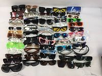 Overview of assorted sunglasses and eyeglasses frames spread on white background, showing various styles and colors.