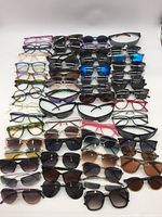 Top-down photo showing multiple rows of assorted sunglasses and eyeglasses frames in various colors and styles laid flat on a white surface