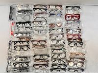 Overview of assorted eyeglasses frames arranged in rows, some in plastic packaging, showing variety of styles and colors.