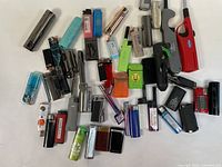 Full lot of assorted collectible butane lighters shown in a group on white surface