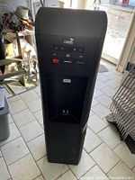 Front view of black Oasis water dispenser showing the control panel with buttons for hot, room, and cold water dispensing and a water outlet below.