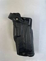 Side view of black Safariland holster showing retention strap and general shape.