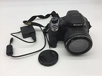 Sony Cyber-Shot DSC-H400 bridge camera with lens cap and charger cable shown on white background