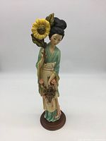 Front view of the figurine showing the Japanese girl holding a large sunflower and standing on a round brown base.