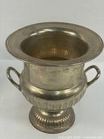 Front left angle view of the silver tone pedestal ice bucket showing the flared rim, urn body, and side handles.