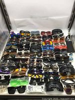 Top-down view of multiple rows of assorted sunglasses arranged in a display box showing different frame shapes and lens colors.